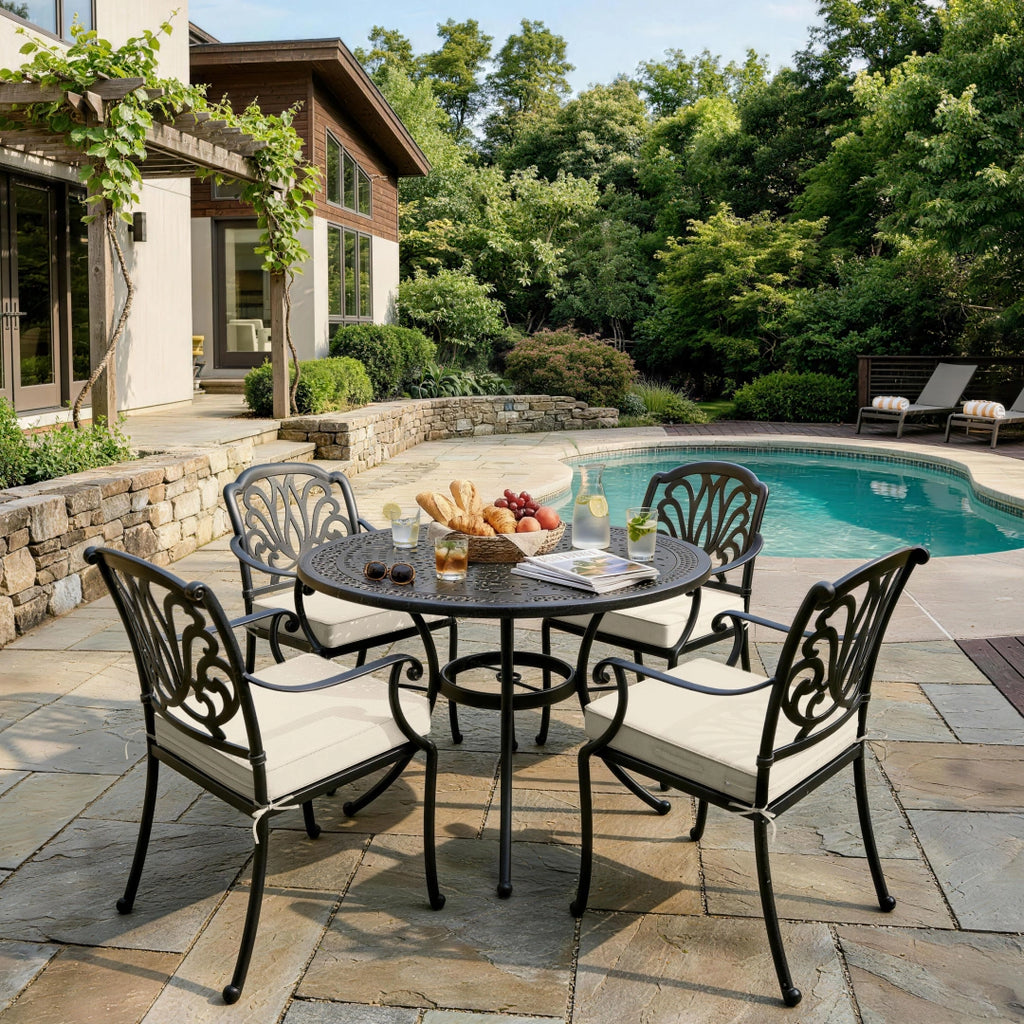 outdoor seat cushions in cream on black metal patio dining chairs, shown around a round table beside a sunny backyard pool