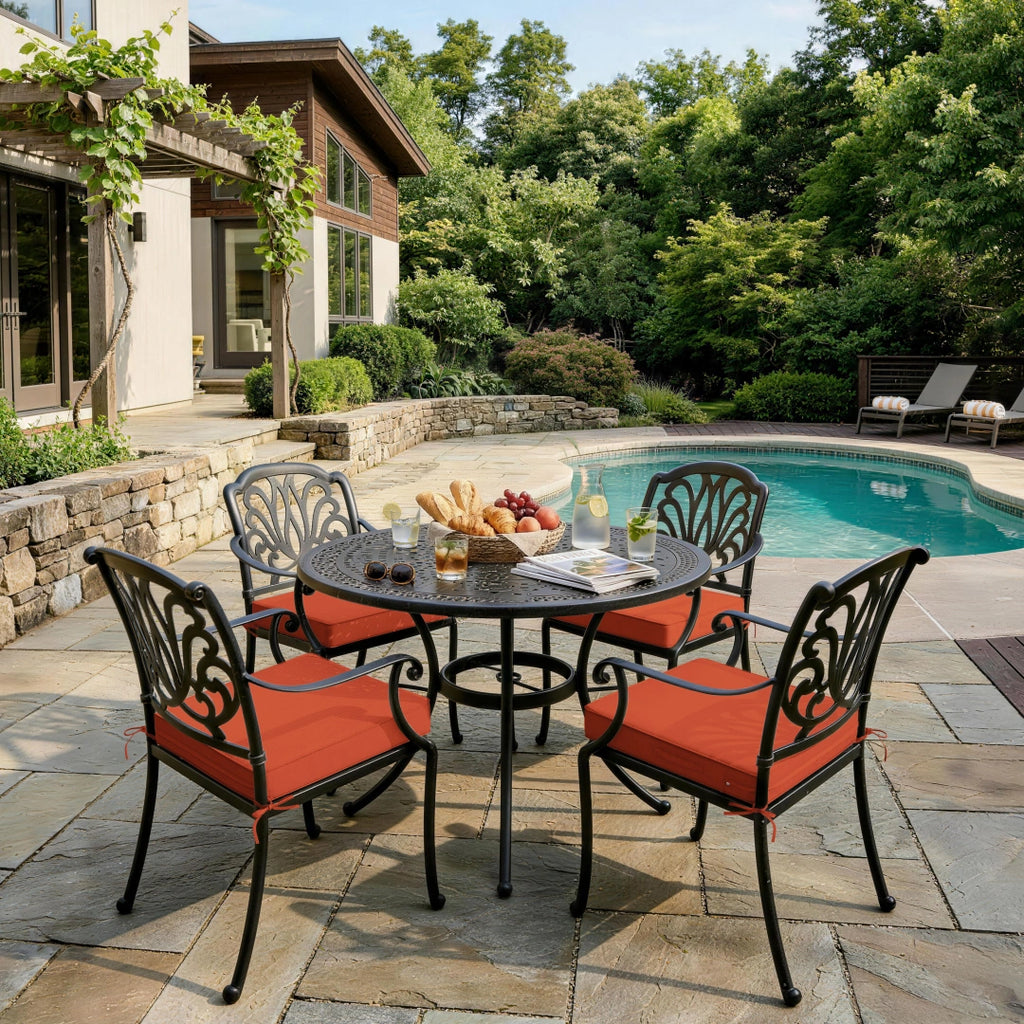 outdoor seat cushions in orange on black metal patio dining chairs, shown beside a pool with a round outdoor table